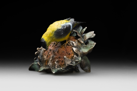 Photo of table top bronze sculpture of Gold Finch pulling seed from sunflower with multiple colors of patina and portions of exposed bronze