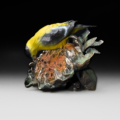 Photo of table top bronze sculpture of Gold Finch pulling seed from sunflower with multiple colors of patina and portions of exposed bronze