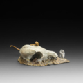 Photo of bronze sculpture of lizard on animal skull amongst flat rocky terrain