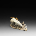 Photo of bronze sculpture of lizard on animal skull amongst flat rocky terrain